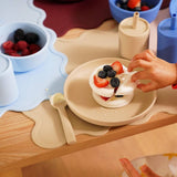 Child's hand reaching for a dessert on a plate with a wooden table setting.