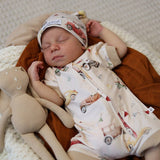 A sleeping newborn baby wearing a cream-colored zip-up onesie and matching hat with a vintage car print, lying on a brown blanket next to a beige stuffed bunny.