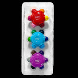 Three Ooly baby teething toys in a clear plastic blister pack on a black background. The toys are red, blue, and purple, each with multiple colorful protruding nubs.