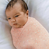 Newborn baby wrapped in a pink blanket with heart patterns on a white background