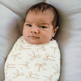 Newborn baby wrapped in a white blanket with brown patterns, lying on a soft surface.