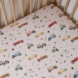 Crib with a patterned mattress cover featuring vintage cars and toys.