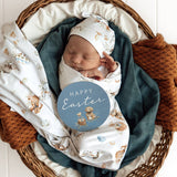 Newborn baby wrapped in a blanket with Easter-themed design, surrounded by cozy blankets in a basket.