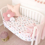 Crib with floral bedding, pink pillow, and soft pink blanket in a nursery setting.