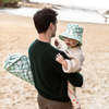 Man holding a child on a beach with a green checkered bag.