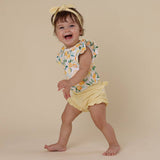 Child wearing a floral top and yellow bloomers on a beige background