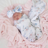 Newborn baby wrapped in floral fabric with a matching headband, surrounded by pink blankets.