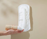 Hand holding a white sanitary pad and a brown bottle against a beige background