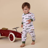 Child wearing pajamas with car patterns standing next to a red toy car on a beige background