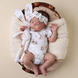 Newborn baby in a basket with a soft toy and floral headband, on a beige background