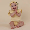 Baby in a yellow outfit and headband sitting on a beige background