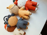 A group of colorful, stylized clay or plastic doll figures arranged on a plain white surface.