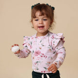 Child wearing a floral shirt with ruffled sleeves against a beige background