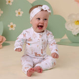Baby wearing a white outfit with animal prints and a matching headband, sitting against a floral background.