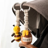 Plush bee and honeycomb toy hanging from a stroller handle.