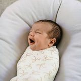 Newborn baby wrapped in a white blanket with brown patterns, lying on a soft beige pillow.