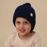Child wearing a navy blue knit beanie with a pom-pom on a beige background