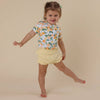 Child wearing a floral shirt and yellow shorts on a beige background