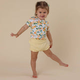Child wearing a floral shirt and yellow shorts on a beige background