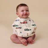 Baby wearing a bib with car patterns on a beige background