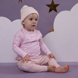 Child wearing a pink outfit with stars, sitting on a cloud-like surface against a purple background with stars.