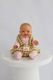 Baby doll in a checkered outfit on a white pedestal with a white background