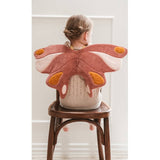 Person wearing a butterfly-shaped pink and orange plushie on their back, sitting on a wooden chair.