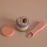 Pink nail clipper with a jar of nail clippings on a beige background