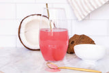Glass of pink drink with a straw on a marble surface with coconuts and a bowl.