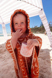 Child in an orange hooded towel on a beach