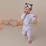 Child in a floral onesie standing in front of balloons on a beige background