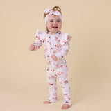 Baby wearing a floral onesie and headband on a beige background
