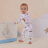 Baby in a patterned outfit standing next to a toy chest with an anchor design on a beige background