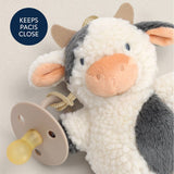 Plush cow toy with a pacifier attached on a light background