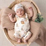 A baby lying on their back inside a woven rattan bassinet, wearing a cream-colored nautical-themed romper and matching hat. The romper features illustrations of a pirate, ship, and sea creatures.