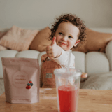Child sitting on a couch with a glass of juice, a bag, and a package on a table.