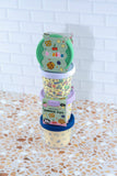 Stack of colorful snack pots on a speckled countertop with a white tiled wall background.