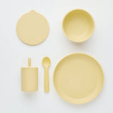 Set of yellow ceramic dishes including a bowl, plate, cup, and spoon on a white background