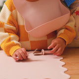 Child wearing a pink bib and yellow and white striped sweater, playing with toys on a wooden floor.