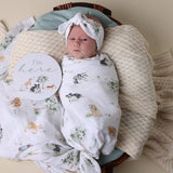 Newborn baby wrapped in a floral blanket with a headband, lying on a soft surface.