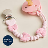 Pink silicone pacifier clip with bow designs on a beige background