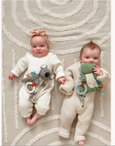 Two babies in knitted outfits with toys on a textured rug