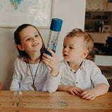 Two children sitting at a table with a water bottle, in a home setting.