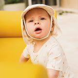Baby wearing a light-colored bonnet sitting on a yellow surface.
