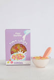 Tiny Harlow cereal box with a bowl of cereal and spoon on a light gray background