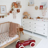 Nursery room with wooden crib, white dresser, and red toy car.