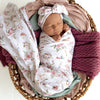 Newborn baby wrapped in floral blanket with matching headband in wicker basket