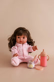 Doll in pink outfit with baby care items on a beige background