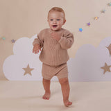 Baby in a beige outfit standing against a backdrop with clouds and stars.