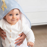 Baby wearing a white outfit with a blue hood featuring giraffe designs, held by an adult.